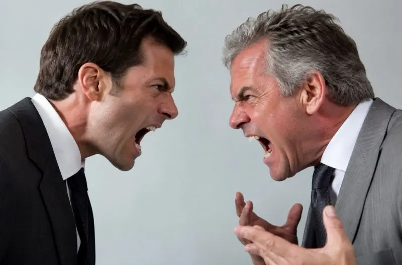 Due uomini in abiti da lavoro si guardano in faccia urlando, in un confronto teso che rappresenta il conflitto irrisolto nelle organizzazioni.