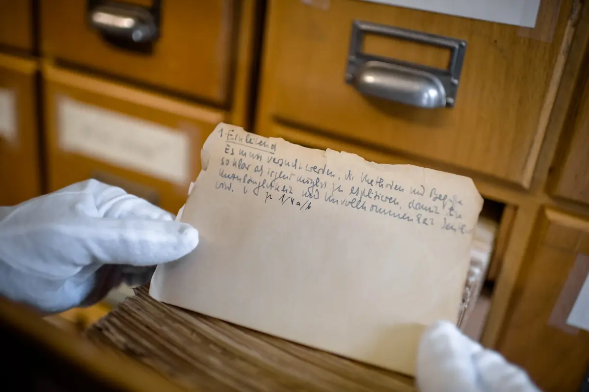 Una scheda archivistica manoscritta in un cassetto di legno, tenuta con guanti da archivista